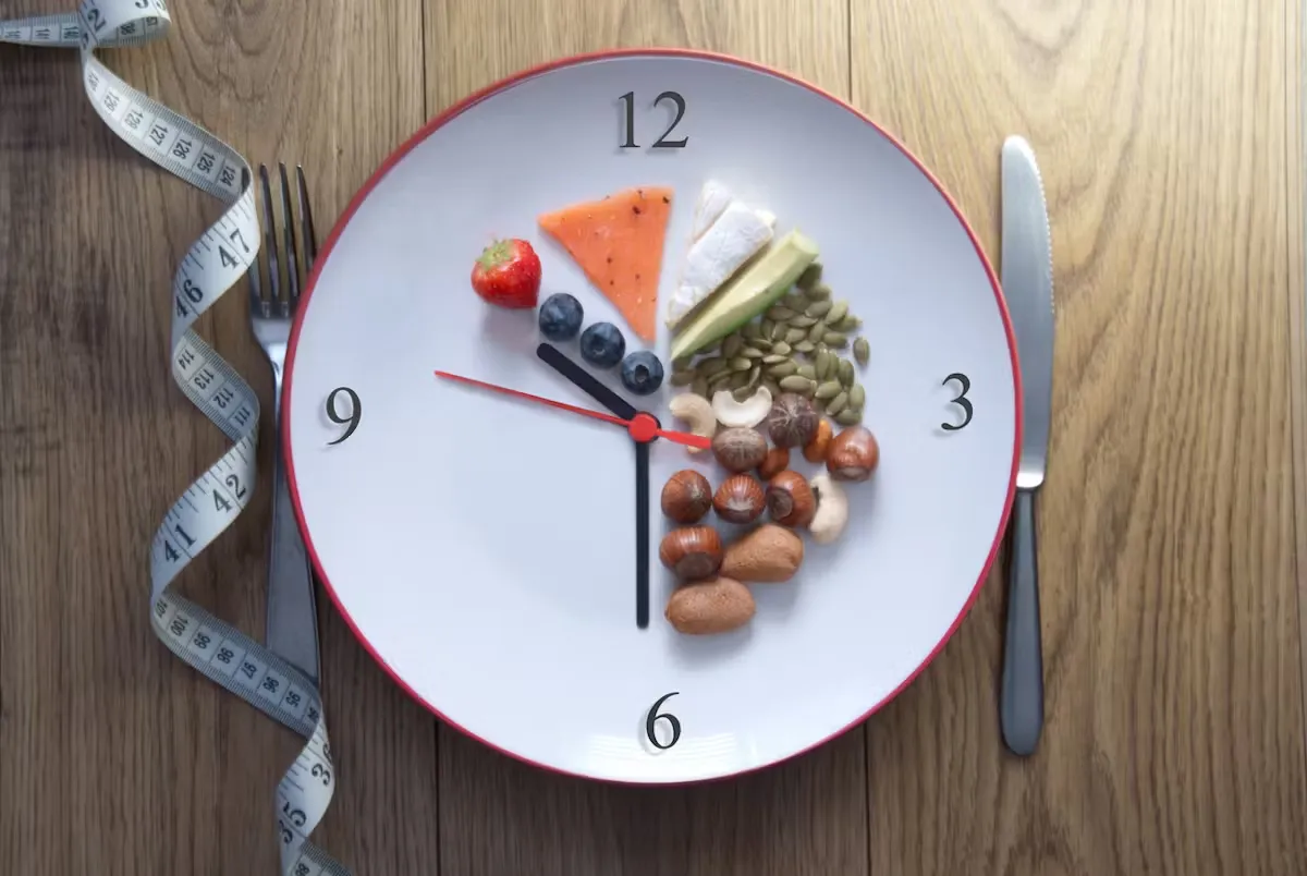 Une assiette en forme d'horloge avec des aliments comme fraise, myrtilles et noix. Fond en bois, ruban à mesurer enroulé autour d'une fourchette.